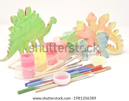 Two wooden mock-ups of dinosaurs, acrylic paints and creative brushes isolated on a white background