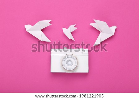 White painted camera and origami doves on a pink background. Minimalism