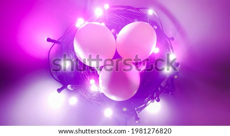 Creative concept photo of Easter chicken bird eggs in bird nest made with glowing colorful decoration led light bulbs and electric wire with pink background and copy space for text. Close up top view.