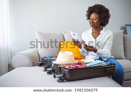 Woman with suitcase packing for holiday at home, coronavirus concept. Woman with antiseptic, wheel bag, air tickets, medical mask, spf, bikini and covid passport packing trolley bag at home