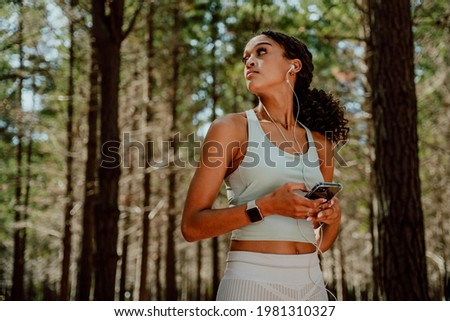 Mixed race female exercising in forest listening to music with earphones 