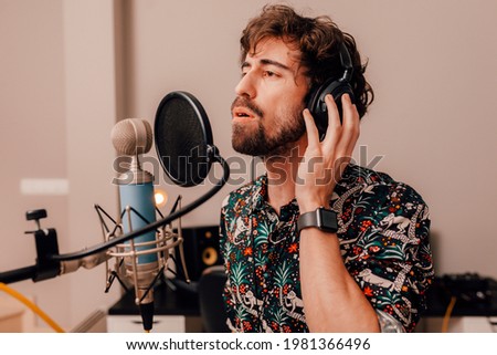 Young caucasian musician singing into microphone while working on songs during a recording studio session at home