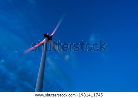 Wind turbine producing renewable green energy against the background of the blue night sky. Copy space, motion blur. Royalty-Free Stock Photo #1981411745