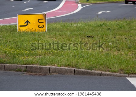 Yellow traffic sign for redirection on urban streets forces navigation system to calculate a new route for correct routing to reach your destination on German roads lying on grass after heavy storm