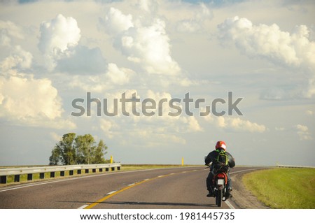 Lonely motorcyclist drives on a road that turns to the right and a sky full of clouds in the background Royalty-Free Stock Photo #1981445735