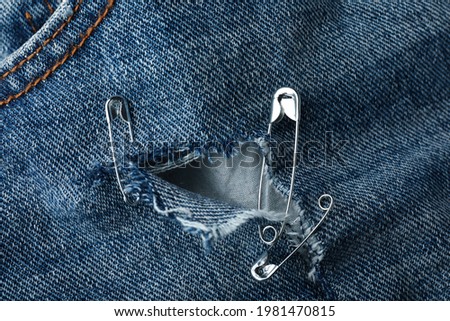 Hole in denim fabric fixed with metal safety pins, closeup Royalty-Free Stock Photo #1981470815