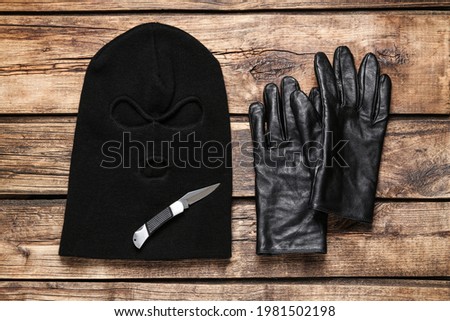 Black knitted balaclava, gloves and knife on wooden table, flat lay