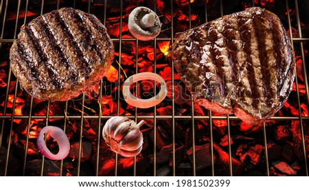 Two grilled beef steaks on bbq grate over hot pieces of coals. Top view.
