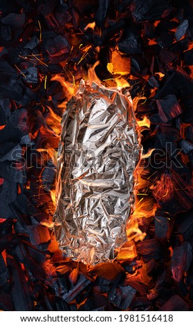 Some food in aluminum foil on grate over hot pieces of coals. Top view.