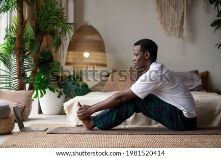 African young man sitting in paschimottanasana or Intense Dorsal Stretch pose, seated forward bend posture Royalty-Free Stock Photo #1981520414