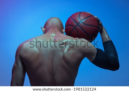 Back view. Portrait of athletic african-american male basketball player posing isolated in neon light on blue background. Concept of healthy lifestyle, professional sport, hobby. Power and force