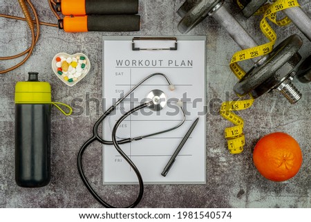 Healthy lifestyle powerlifting workout concept with grip cast iron olympic weight plates on a cement floor. Clip board with workout plan tab. Royalty-Free Stock Photo #1981540574