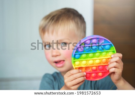 Cute child boy playing with antistress pop it fidget toy. Kid holding trendy silicone pressure relieving sensory board game simple dimple. Royalty-Free Stock Photo #1981572653