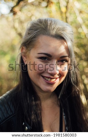 Smiling young woman with black and white hair in a forest.