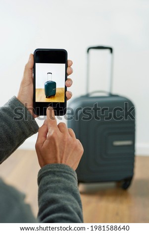 a young caucasian man takes a picture, with his smartphone, of a suitcase to sell it on an online marketplace app designed to sell and buy secondhand goods