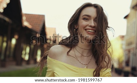 positive young woman with wavy hair smiling outside