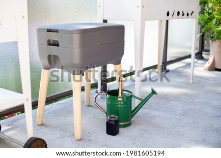 A vermicomposting system (worm composter) sits on an apartment balcony with other patio planters. Worms eat food scraps and produce worm castings and worm tea to be used as fertilizer. Redirect waste.