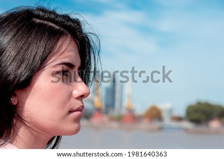close-up of an attractive girl's face, looking diagonally across the street, in daytime, in an urban and industrial environment, with business buildings and offices in the background. business concept