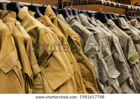 Photo of olive colored military shirts and ripstoprs hanging in military store rack. Royalty-Free Stock Photo #1981657748