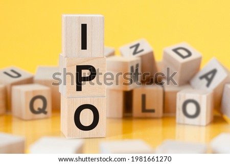 wooden cubes with letters IPO arranged in a vertical pyramid, yellow background, reflection from the surface of the table, business concept. ipo - short for Initial Public Offering