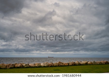A beautiful, dramatic sky over the ocean. A lawn and stones in a wave breaker in the foreground. Picture from Malmo, Sweden