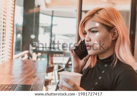A young asian woman argues with her client on the phone while at a coffee shop.