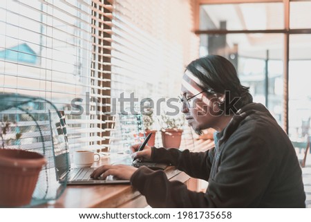 A middle aged asian graphic designer freelancer with a laptop and drawing tablet. Working remotely at a coffee shop or coworking space.