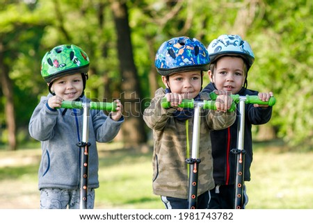 Triplets boys, compete in riding scooters, outdoor in the park Royalty-Free Stock Photo #1981743782