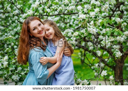 Mother and little daughter hugging each other and walking in blooming apple garden. Mom loves her child. Spring story. Happy family in beautiful spring day.