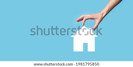 Male hand holding house icon on blue background. Property insurance and security concept.Real estate concept.Banner with copy space
