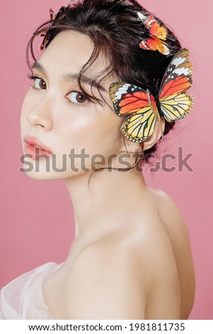 Asian woman has a lovely face is feeling confident with her perfect skin. She took a picture with a butterfly. isolated pink background. Skincare, cosmetology and plastic surgery concept