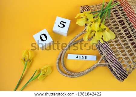 Calendar for June 5: cubes with the numbers 0 and 5, the name of the month of June in English, yellow irises with a wicker basket on a yellow background, top view