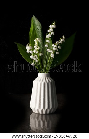 Still life with lilies of the valley in a white vase on a black background. Copy space.