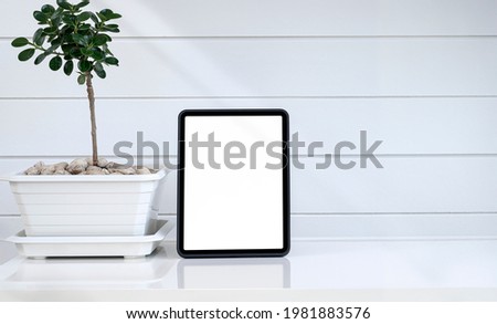 Mockup blank screen tablet in vertical view and plant on white table with copy space.