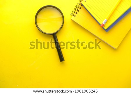 open book and magnifying glass on yellow background .