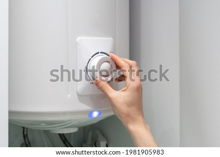 Cropped photo of female adjusting temperature on bathroom electric boiler hanging on wall, using control knob. Water heater in modern apartment Royalty-Free Stock Photo #1981905983