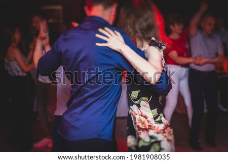 Couples dancing traditional latin argentinian dance milonga in the ballroom, tango salsa bachata kizomba lesson in the red, purple and violet lights, dance festival  Royalty-Free Stock Photo #1981908035