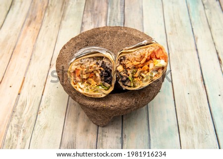 Big grilled chicken burrito inside a gray volcanic stone molcajete on wooden table