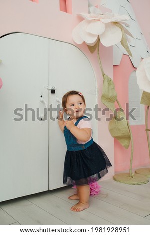 Little cute girl celebrates her birthday at 1 year old. Little girl smiles and crawls against the background of number one, fairy flowers and a pink wall