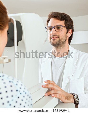 Ophthalmologist In Exam Room With Woman Sitting In Chair Looking Into Eye Test Machine
