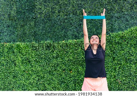 A woman stretches the fitness band. Green rubber for exercise. Outdoor workout. Healthy and sporty active lifestyle concept.