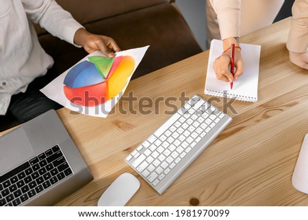 Portrait of multiracial business people holding negotiations, sign a contract. Confident employees having important meeting, looking through important graphs, come to agreement, collaboration concept.
