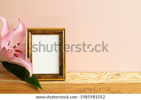 Empty picture frame with lily flower on wooden table. pink background