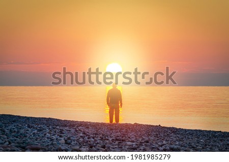 Silhouette of a man stands on the seashore in the light of sunset sun.  Search for God concept. Defocused photo with blur in motion.