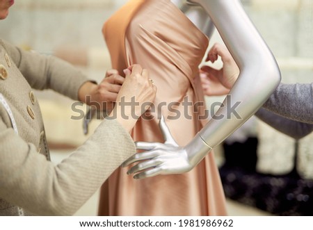 Fashion, dressmaking or tailoring concept. Professional team of tailors, dressmakers or designers working with new model applying linen fabrics beige cloth on mannequin or dummy in atelier Royalty-Free Stock Photo #1981986962