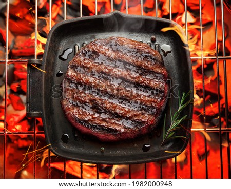 Roasted filet mignon beef steak on bbq pan over hot pieces of coals. Top view.