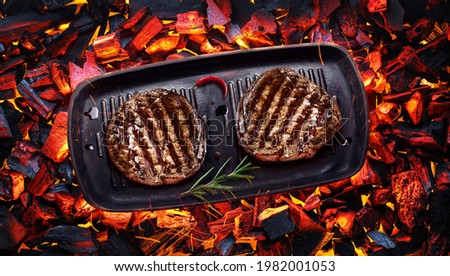 Two grilled filet mignon beef steaks on bbq pan over hot pieces of coals. Top view.