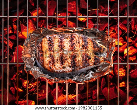 Roasted salmon steak in aluminum foil on bbq grate over hot pieces of coals. Top view.