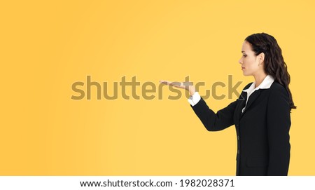 Profile side of beautiful businesswoman showing adverting something or copy space for product. Brunette woman looking at her hand in business studio concept, isolated over orange yellow background.