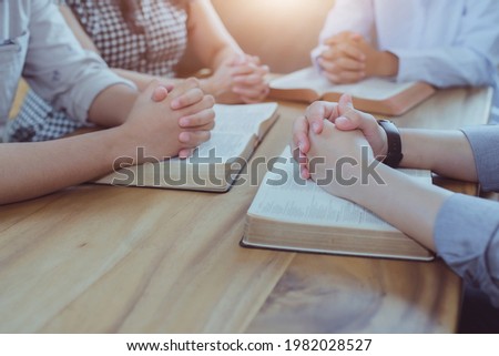 Christian small group  praying on  blurred open bible page on a wooden table while studying the bible together in homeroom, devotional or prayer meeting concept Royalty-Free Stock Photo #1982028527